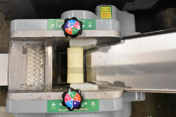 Metal commercial countertop sheeter with adjustable settings, used for rolling dough. Control knobs and directional labels visible.