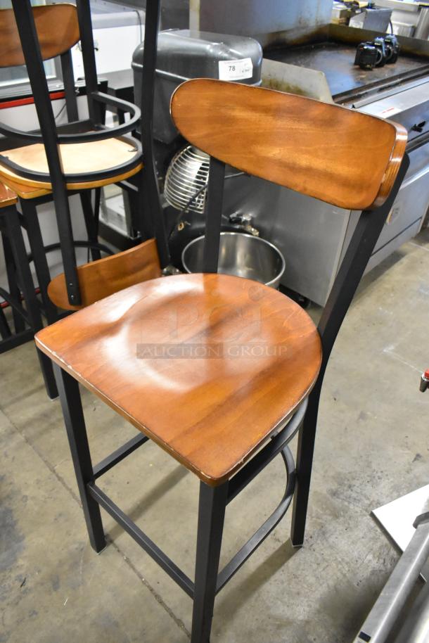Black metal bar-height chair with wooden backrest and seat, sleek design, sturdy, minor wear. Bid includes four chairs.