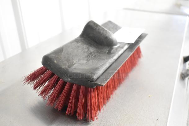 Brand new broom head with red bristles, shows minor scratches and dents. Black base, labeled with inspection tag.