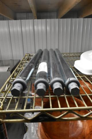 Lot of 4 brand new metal legs, scratch and dent, on a shelf. Each leg has gray caps and visible surface marks.