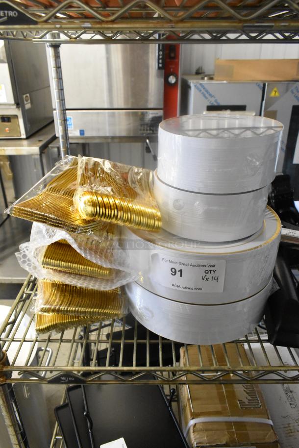 Lot of brand new scratch-and-dent items including paper plates and gold plasticware, neatly stacked on a metal shelf. Label indicates auction details with quantity and source.