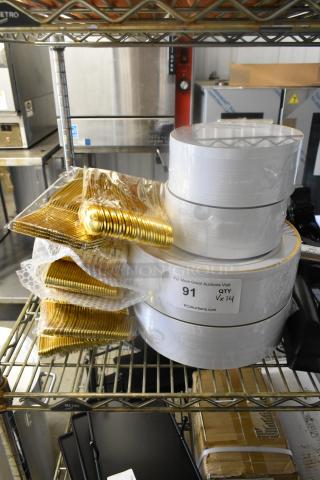 Lot of brand new scratch-and-dent items including paper plates and gold plasticware, neatly stacked on a metal shelf. Label indicates auction details with quantity and source.
