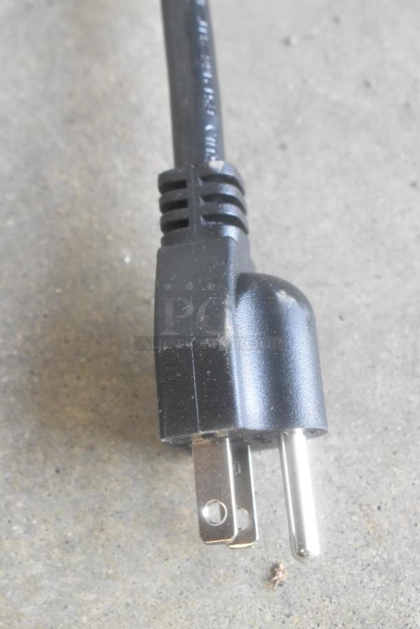 "Black power plug of a Lavex KW-1021B hand dryer on concrete. Shows minor dirt and scratches on prongs."