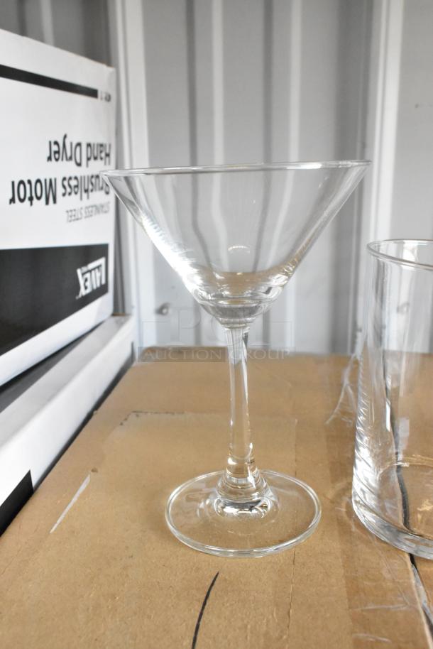 Brand new Acopa 7 oz. martini glass, clear stem design, on a cardboard surface. No visible damage.