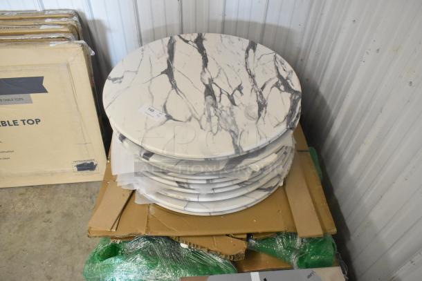 11 brand new round marble pattern tabletops, scratch and dent condition, stacked on cardboard with visible tags.