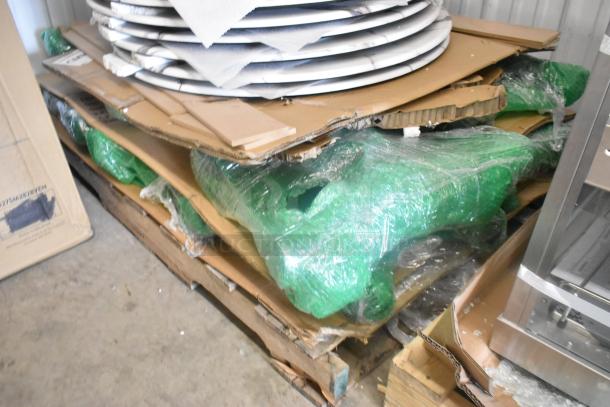 Stack of 11 new scratch and dent items, including round marble-pattern tabletop, wrapped in green plastic on a pallet.