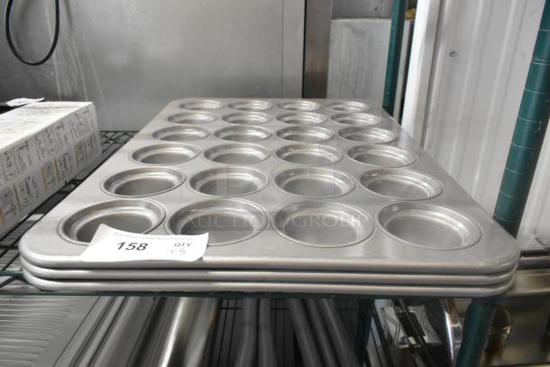 Three brand new 24-cup metal muffin pans, labeled "Scratch and Dent," stacked on a shelf, auction tag visible.