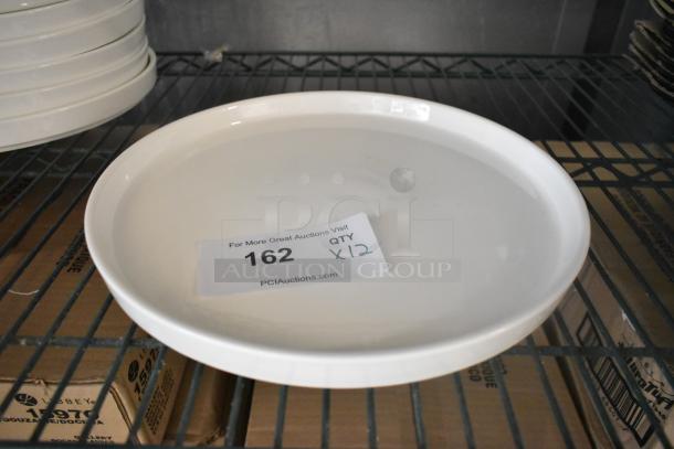 12 new Acopa white plates, scratch and dent condition, on a metal shelf. Auction tag reads "162, QTY x12."