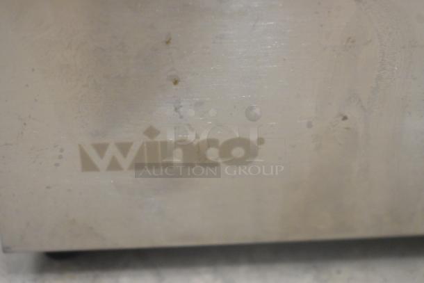 Winco PKTS-2D stainless steel condiment rail, includes 1 pump. Visible brand logo, slightly worn surface. Model: PKTS-2D.