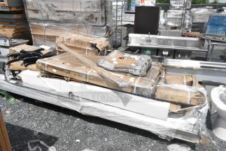 Packaged stainless steel tables labeled as "scratch and dent," 15 new items, wrapped with protective material.