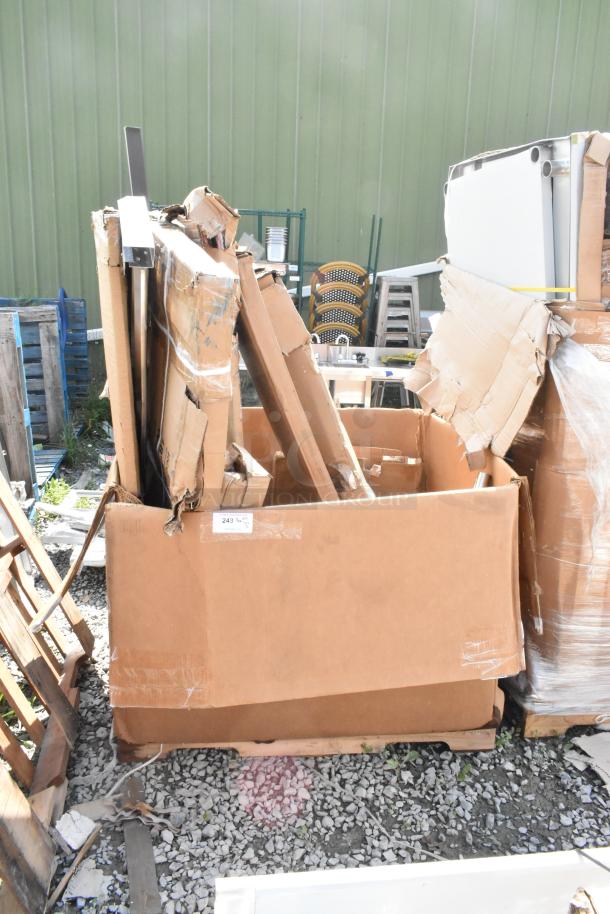 Cardboard box containing assorted new scratch and dent items, including a security cage and stainless tables. Label marked "243."