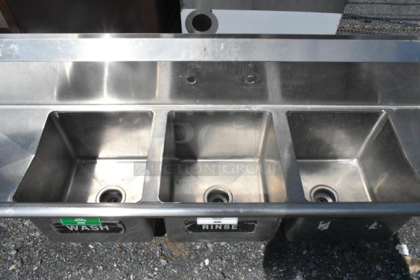 Regency stainless steel 3-bay sink with dual drain boards, no legs. "Wash" and "Rinse" labels on basins.