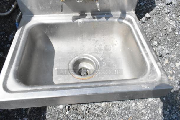 Stainless steel single bay wall mount sink with faucet and handles, used condition, signs of wear visible.