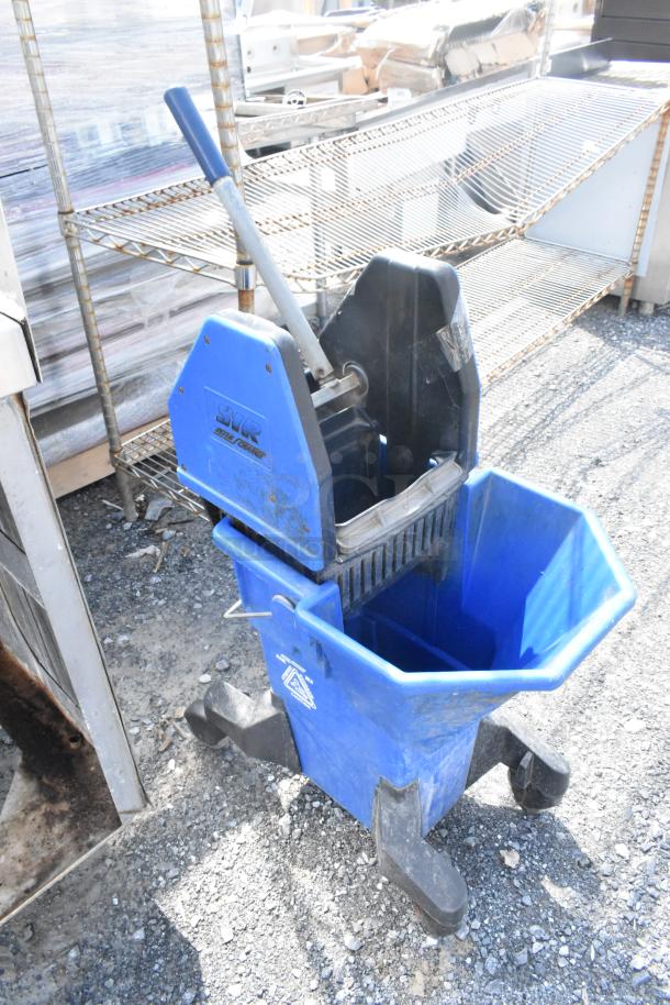 Blue poly mop bucket on casters, marked "SYR", dual compartments, attached wringer, and sturdy handle, showing slight wear.