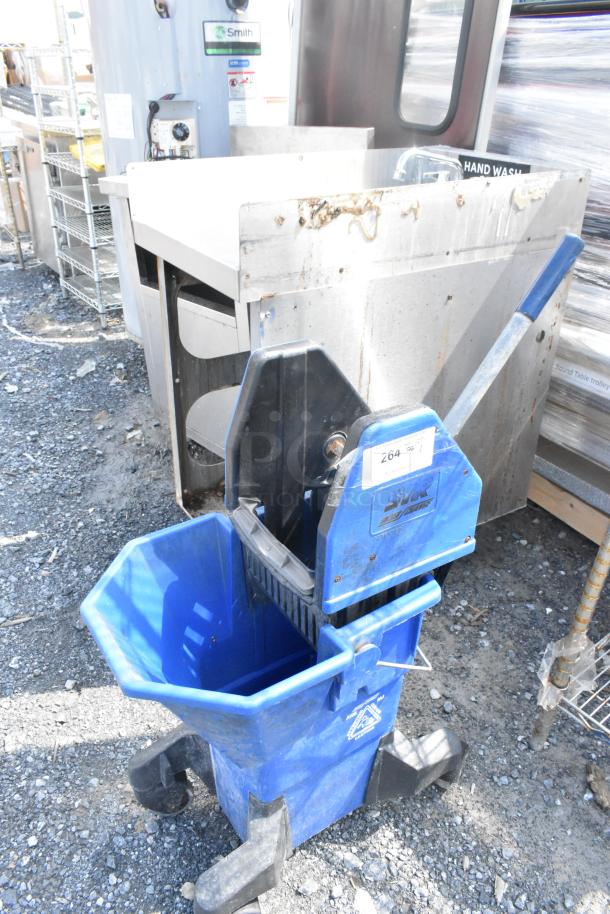 Blue poly mop bucket on casters with side wringer. Visible label indicates model information. Appears in used condition.