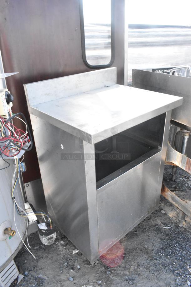 Stainless steel table with a backsplash and open storage space, in used condition. Some wires and plumbing components are visible nearby.