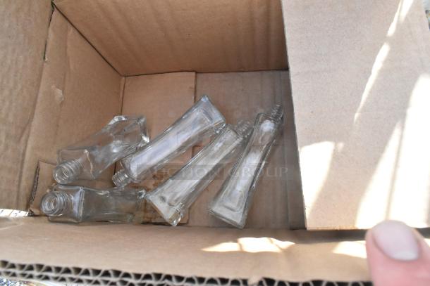 Cardboard box containing several clear, rectangular glass bottles with open tops.