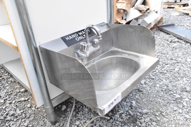 Stainless steel wall mount sink with side splash guards, faucet, and handles. Features "Hand Wash Only" label. Used condition.