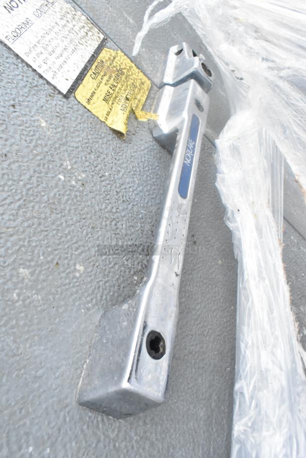 Norlake walk-in freezer handle detail with labels. Features durable metal construction, visible wear, and warning stickers.