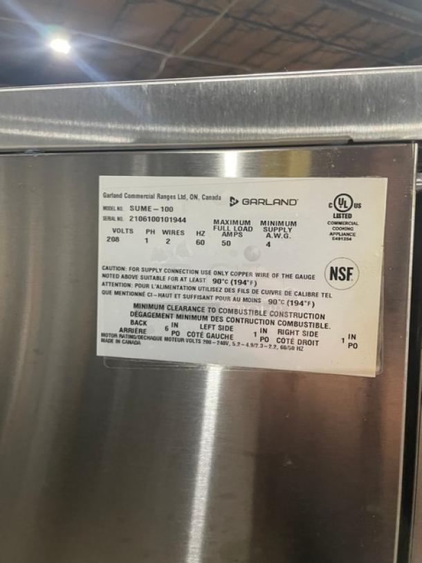 U.S. Range by Garland Summit Series stainless steel single deck convection oven, Model SUME100, with thermostatic controls and wired racks. Serial number 2106100101944, 208V 1 Phase, on legs. UL and NSF listed label visible.