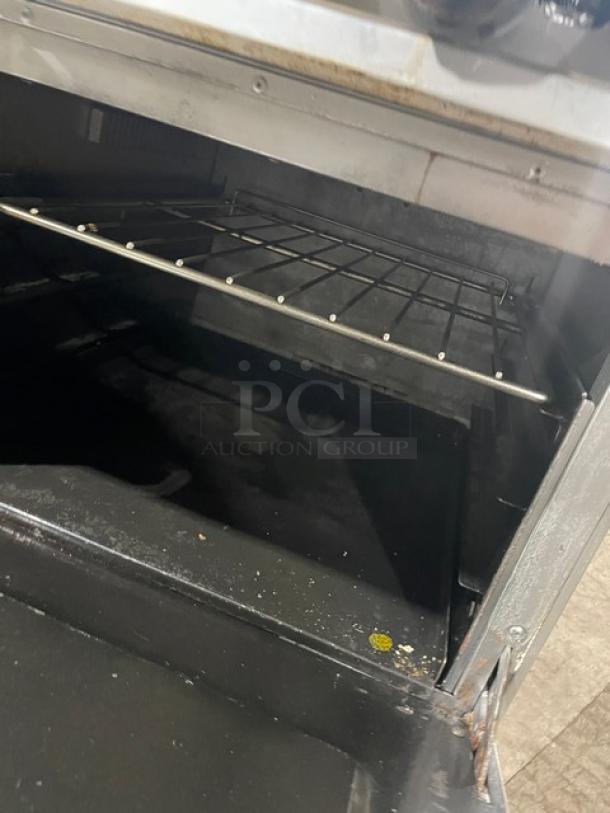 Stainless steel 8-burner range with double oven, wire rack, and backsplash. Standard Range brand, on casters.
