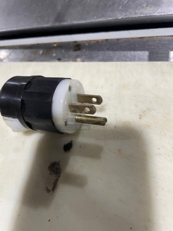 Black and white electrical plug with three prongs, sitting on a cutting board. Plug shows signs of wear.