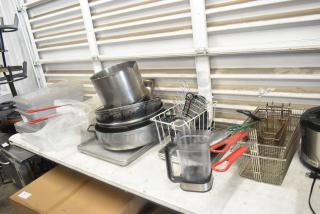 Lot of kitchen items including metal pots, fry baskets, poly bins, and utensils on a table, various conditions visible.