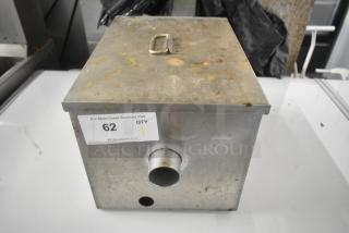 Metal grease trap with visible rust marks, front pipe fitting, and handle on top. Tag indicates auction item 62.