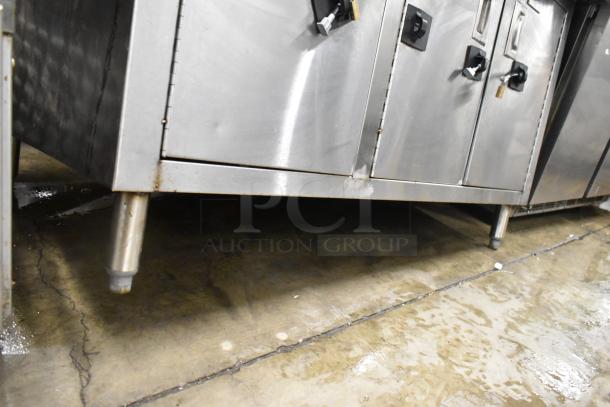 Stainless steel counter with three doors, under-shelf, and sturdy legs. Visible wear but functional for storage.