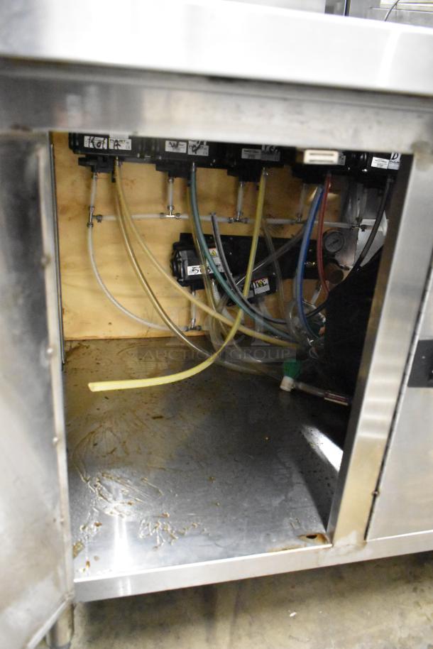 Stainless steel counter with three doors and under shelf, featuring visible piping and storage area, showing signs of wear.