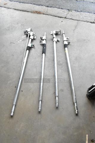Four metal C stands, silver finish, adjustable height, used condition, suitable for photography or video lighting.