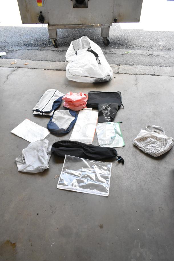 Lot of assorted bags on concrete floor, including mesh bags, drawstring pouches, and clear plastic sleeves. Various sizes and colors.