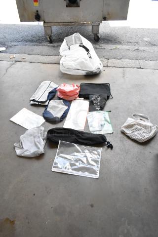 Lot of assorted bags on concrete floor, including mesh bags, drawstring pouches, and clear plastic sleeves. Various sizes and colors.