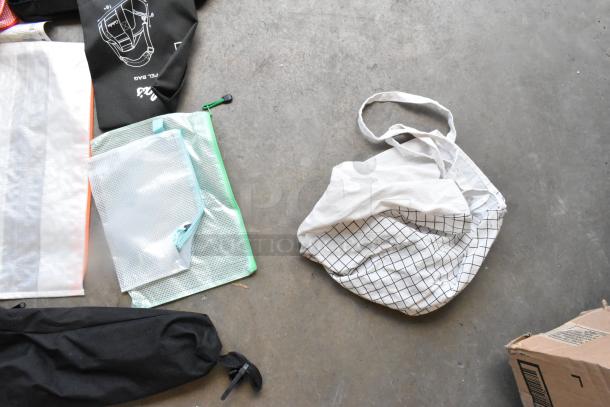 Lot of various bags including white grid tote, black drawstring bag, and translucent zip pouches. Mixed materials, fair condition.