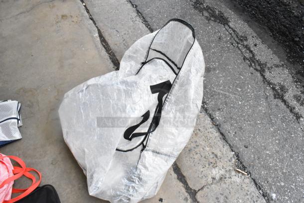 Various bags on pavement, including a large white bag with black print. Mixed condition. Ideal for bulk purchase.