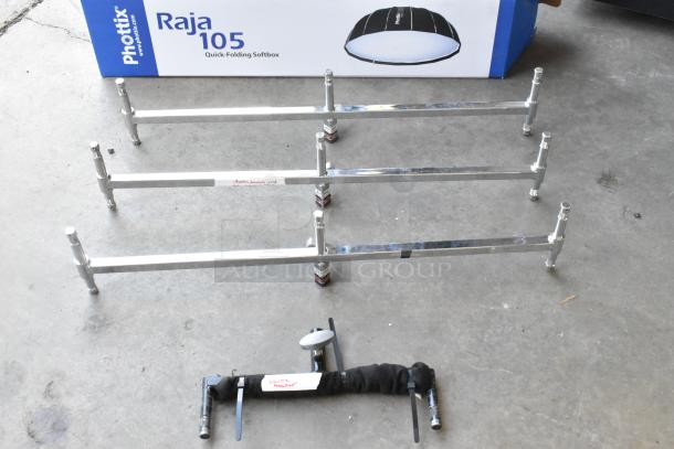 Alt text: Lot of metal pieces including chrome bars and a labeled "Double Header" part, with a Phottix Raja 105 softbox box in background.