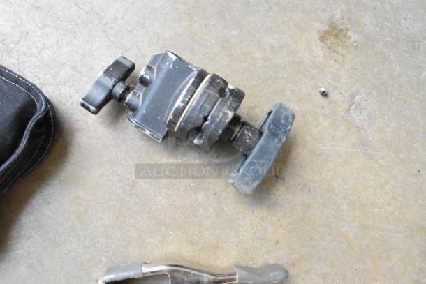 Lot of various clamps in a hard bin, worn condition; includes adjustable clamp with turn knob, visible scuffs and wear.