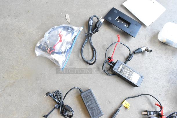 Flanders Scientific Zunzheng BM090 Broadcast Monitor accessories, including power cables and connectors, placed on concrete.