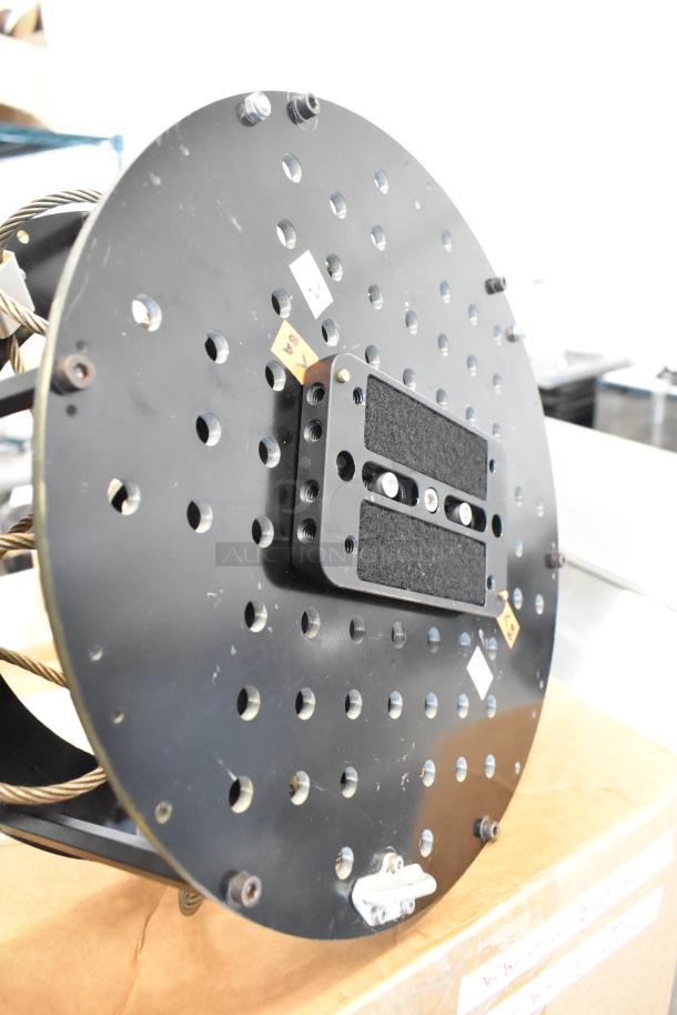 Black round vibration isolator with perforated surface, textured pad, and visible labels. Appears in good condition.