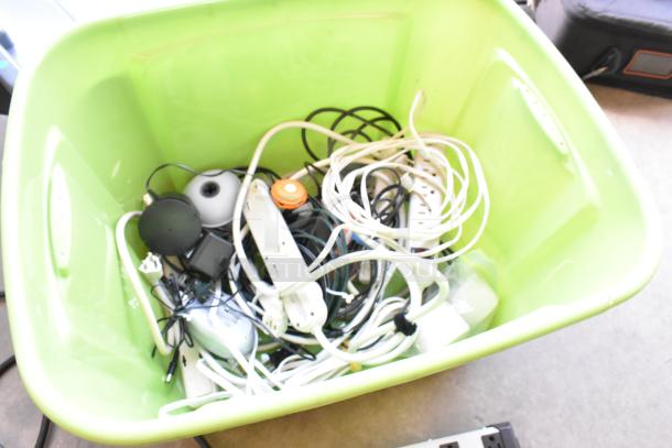 Lot of wiring, power strips, and electronics in a green poly bin; various cables and plugs visible, condition unclear.