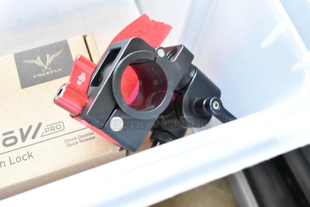 Lot includes Movi Pro Pop-n Lock clamp in black and red, boxed, within a clear poly bin. Marked "25mm Dovetail Quick Release."