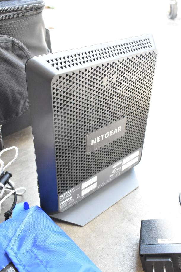 Think Tank soft bag with contents, including a Netgear C7000v2 modem and power adapter. Bag partially visible.