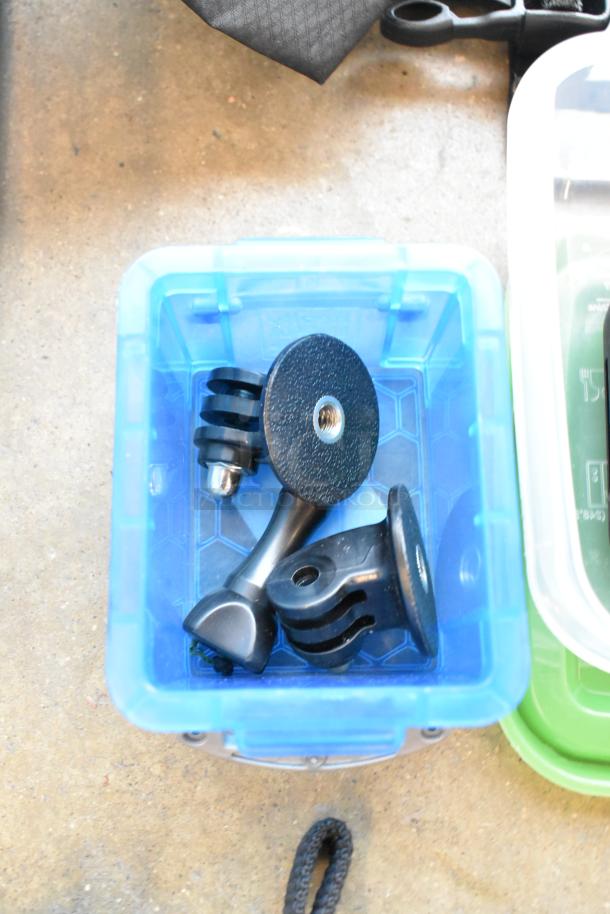 Lot of various items in a blue poly container, including GoPro accessories, wires, and a poly bin on concrete surface.