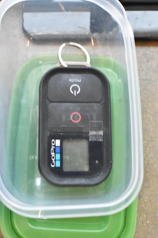 Poly bin containing a GoPro remote with visible buttons and display. Includes various wires and poly containers.