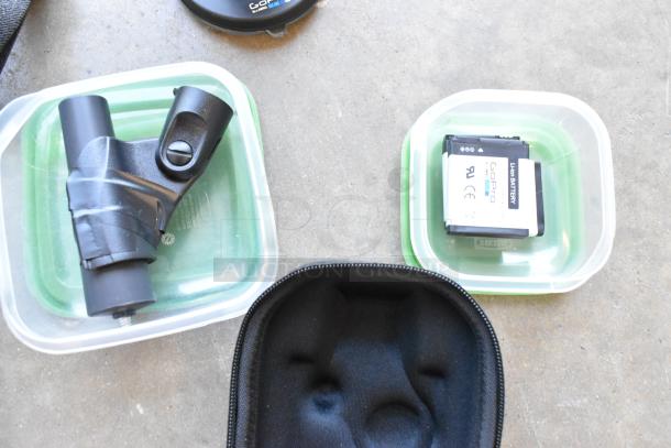 Lot of GoPro accessories, wires, and poly containers in a bin, includes a GoPro battery and padded case, in fair condition.