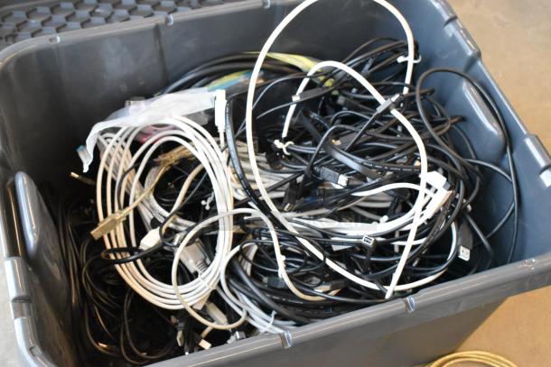 Lot of various cables including black and white wires in a gray poly bin. Mix of USB, HDMI, and other connectors.