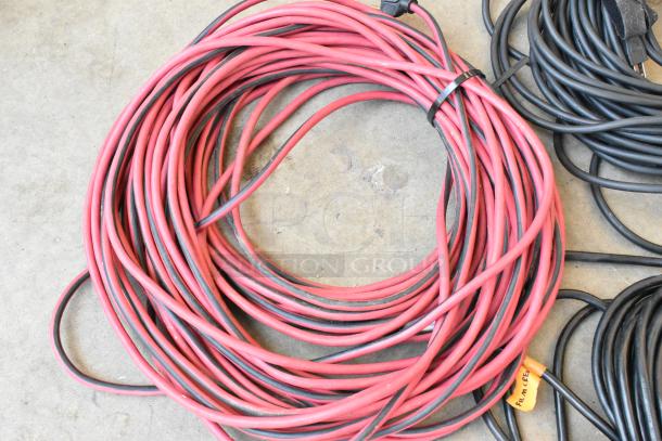 Lot of extension cords in a poly bin, includes red and black cords, various lengths, plastic plug ends, good condition.