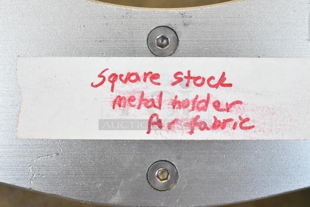Square metal holder labeled "Square stock metal holder for fabric" in red on white paper, attached with screws.
