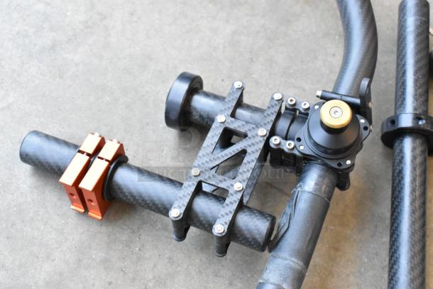 Movi Ring with carbon fiber frame, equipped with batteries. Features orange clamps and adjustable brackets. Suitable for stabilizing camera systems.