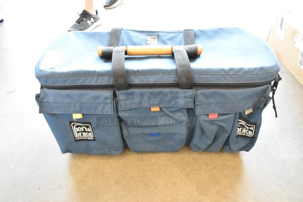 Porta Brace blue bag with Sachtler DV tripod base, features multiple pockets, zipper closure, and carry handle.